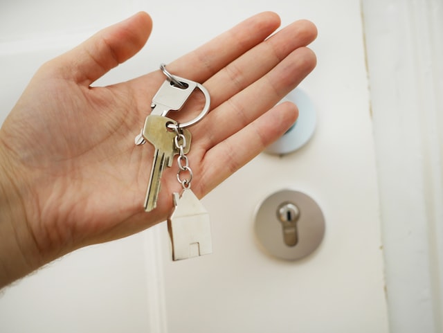 Person Holding Keys with model of a home next to door